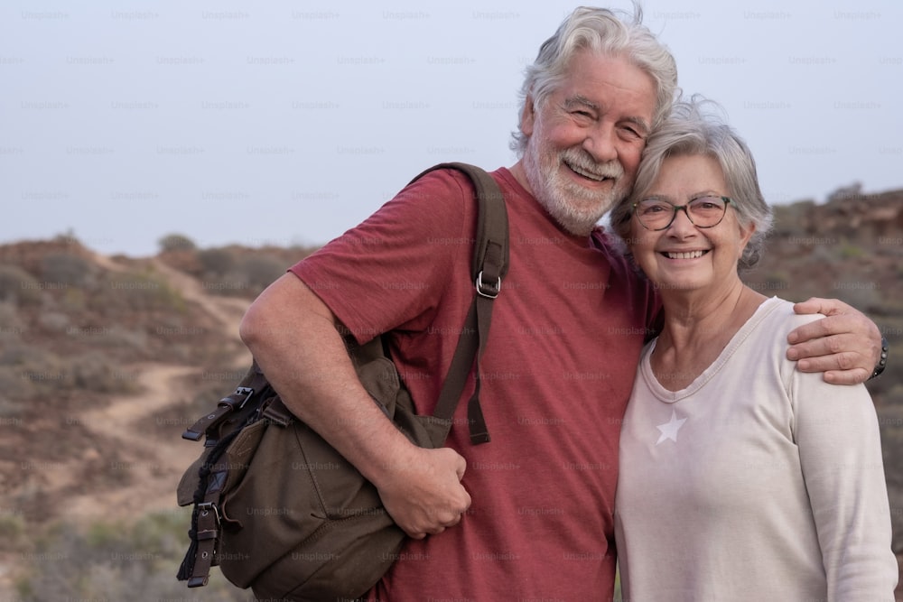 Schönes älteres Paar, das bei Sonnenuntergang auf dem Land spazieren geht, in die Kamera schaut und lächelt