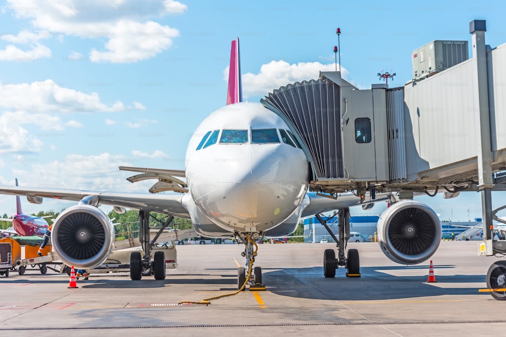 Commercial passenger airplane in the parking at the airport with a nose forward and a gangway - front view. Service and preparation for the flight