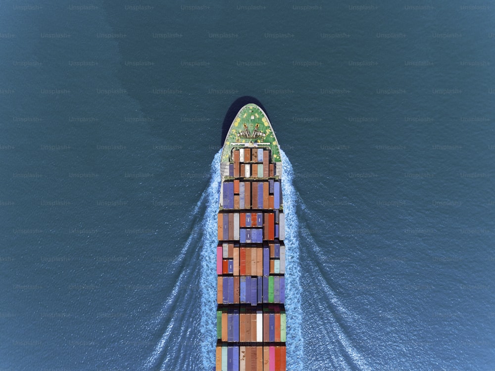 Luftaufnahme Containerschiff mit voller Geschwindigkeit mit schönem Wellenmuster auf dem blauen Meer für Logistik, Import, Export, Versand oder Transport.