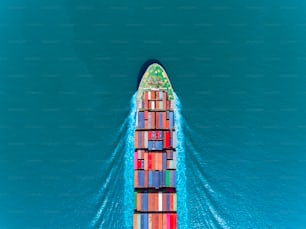 Aerial top view container ship full speed with beautiful wave pattern on the blue sea for logistics, import export, shipping or transportation.
