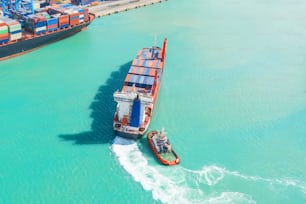 Nave portacontainer in import export e logistica aziendale. Il rimorchiatore accompagna la nave quando entra nel porto mercantile. Veduta aerea