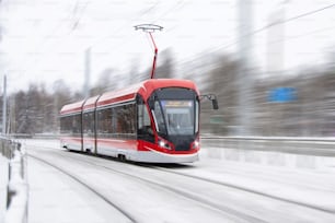 The tram is passing rapidly at a bend in a snow covered city park