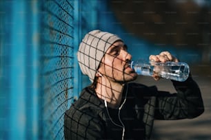 屋外での運動を休んでいる間、目を閉じて水を飲む疲れた運動選手。