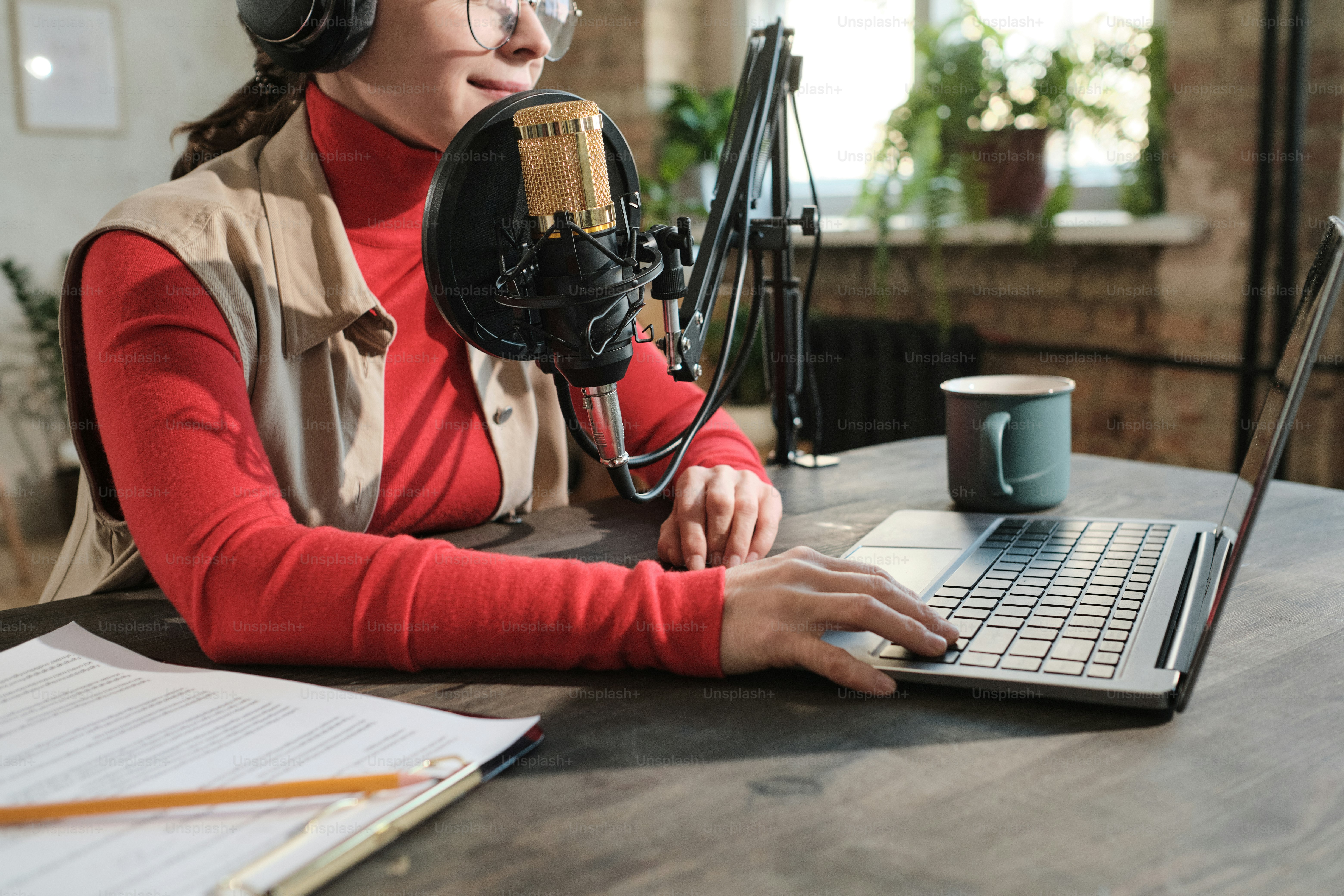 Close-up of woman in headphones sitting at the table and working on laptop in radio studio