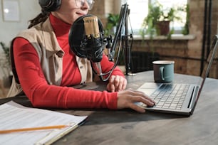 Close-up of woman in headphones sitting at the table and working on laptop in radio studio