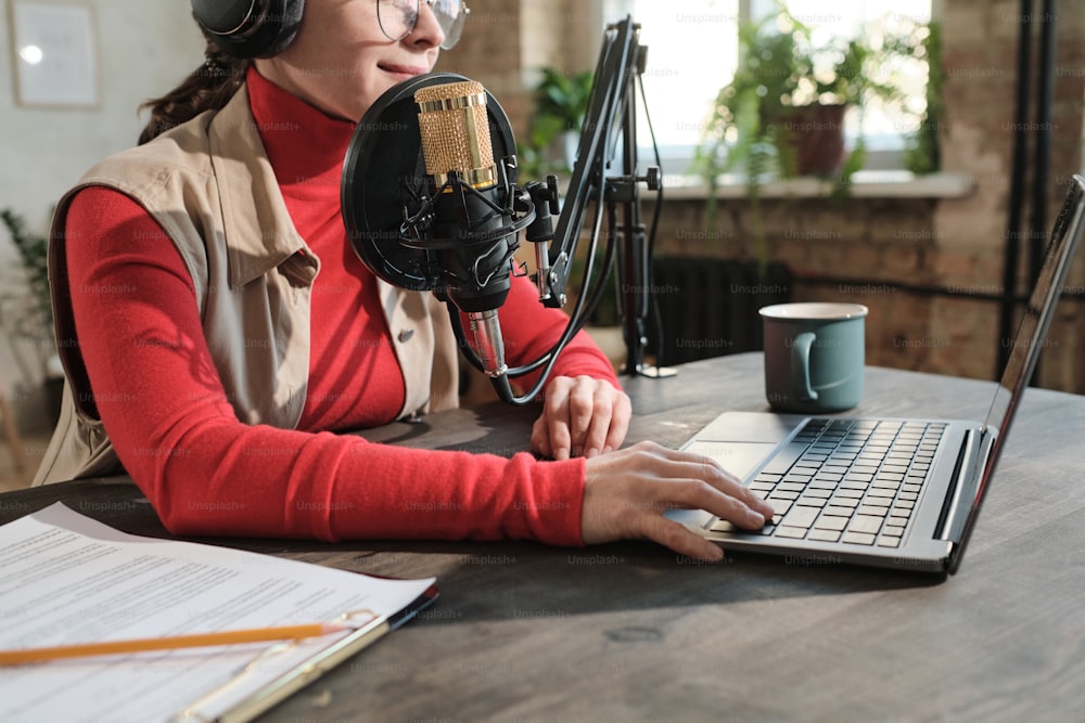Close-up of woman in headphones sitting at the table and working on laptop in radio studio