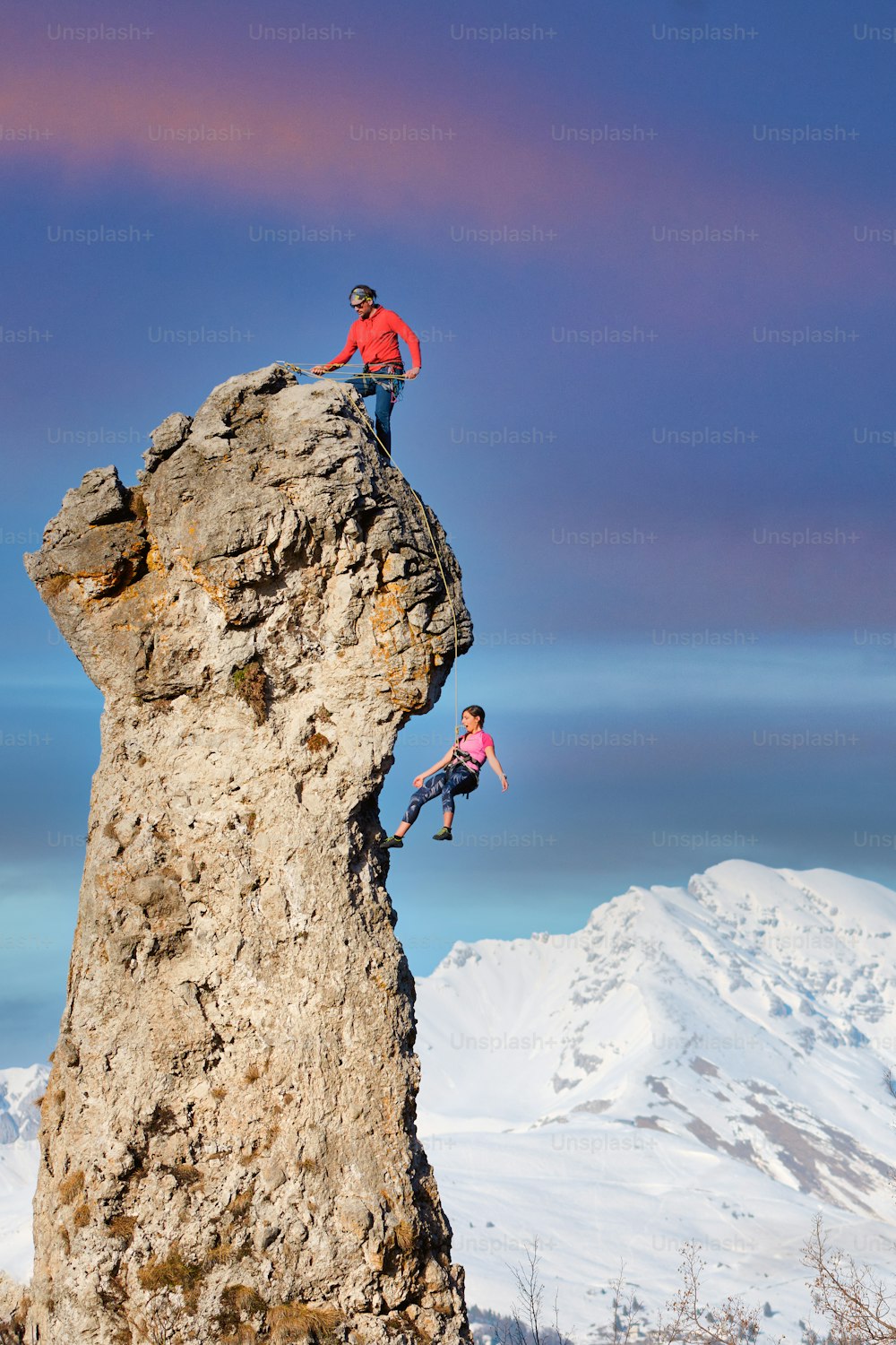 Um alpinista no topo faz seu parceiro descer a corda