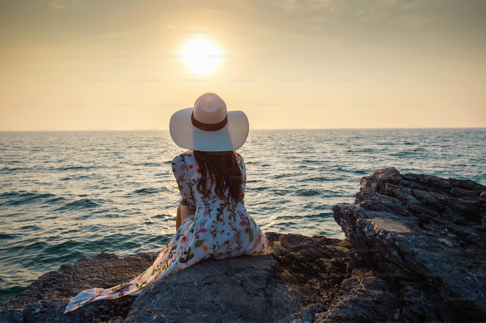 Giovane donna seduta sulla cima della roccia e guardando la riva del mare e il tramonto nell'isola di Si Chang.