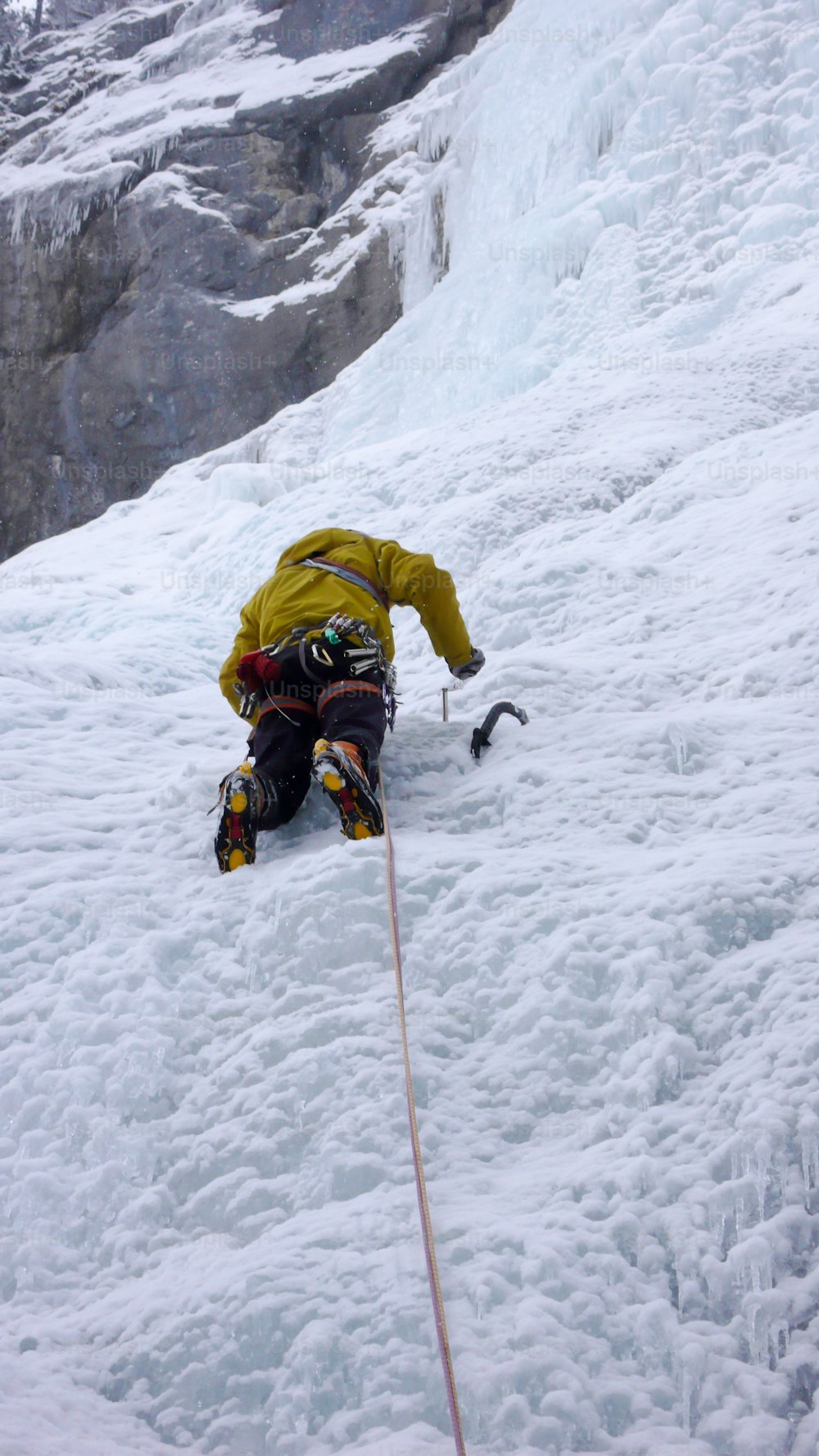 guida alpina maschile che si arrampica su una ripida cascata ghiacciata in una fredda giornata invernale nelle Alpi