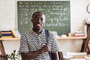 Portrait of African student with backpack smiling at camera while standing in the classroom