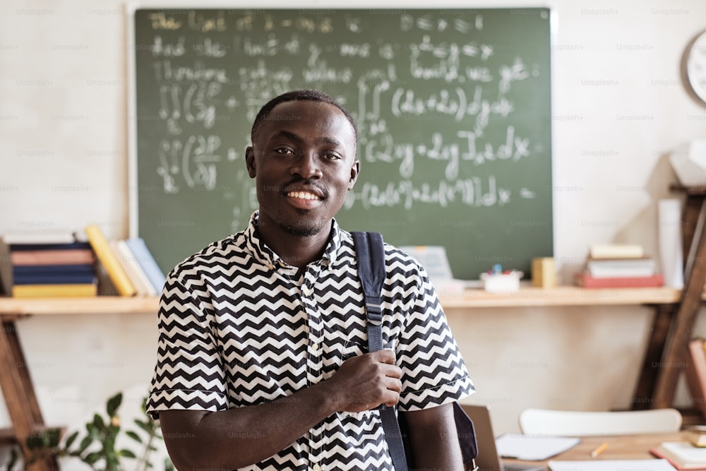 Retrato de un estudiante africano con una mochila sonriendo a la cámara mientras está de pie en el aula