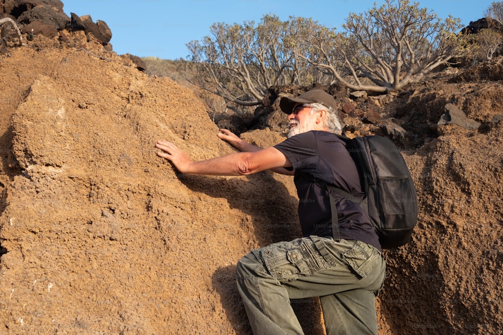 Adult man hiking an arid volcanic mountain. One caucasian people with white hair and beard. Enjoying freedom and adventure. Blue sky on background