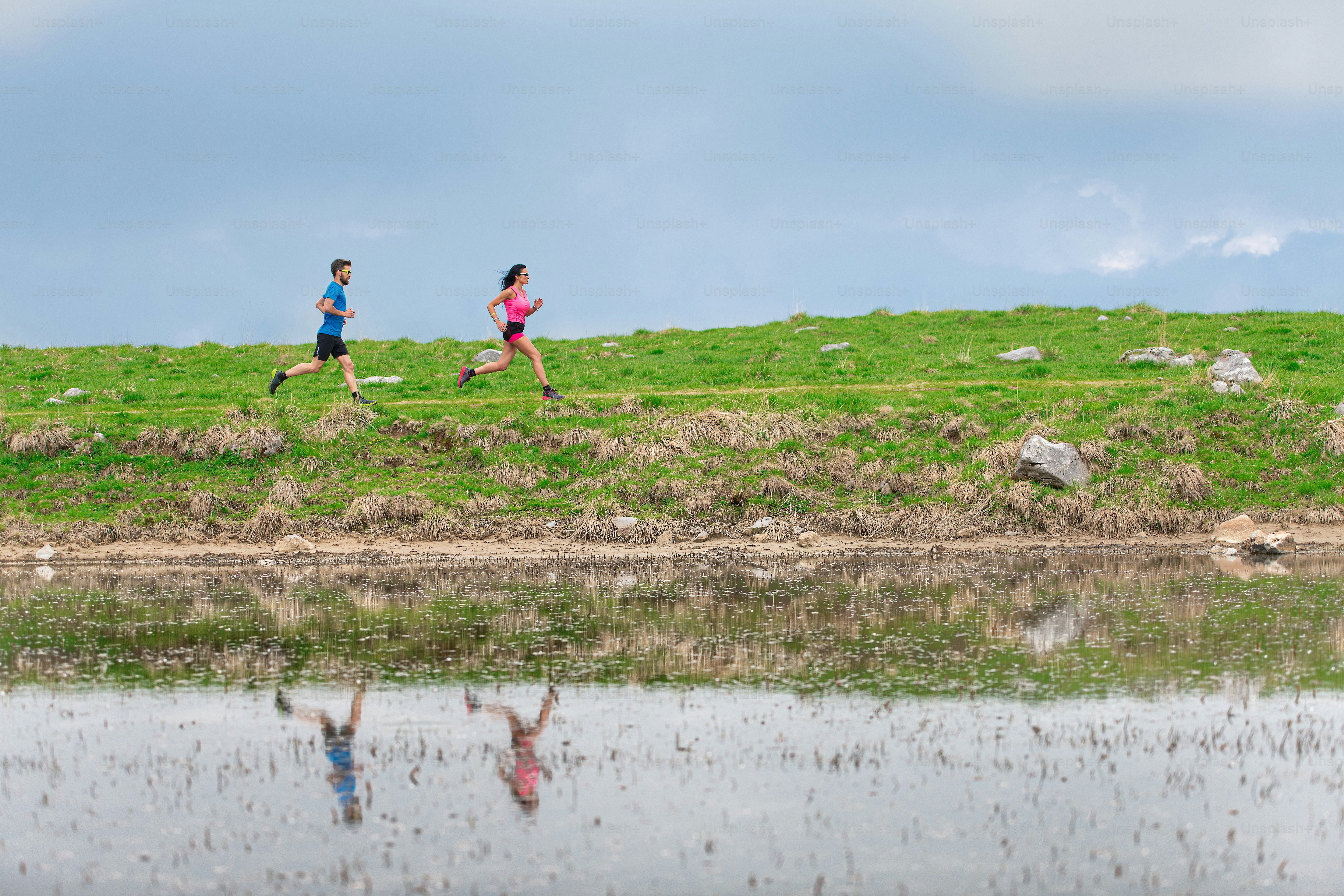 Athletes in training in the mountains are reflected in the lake as they run