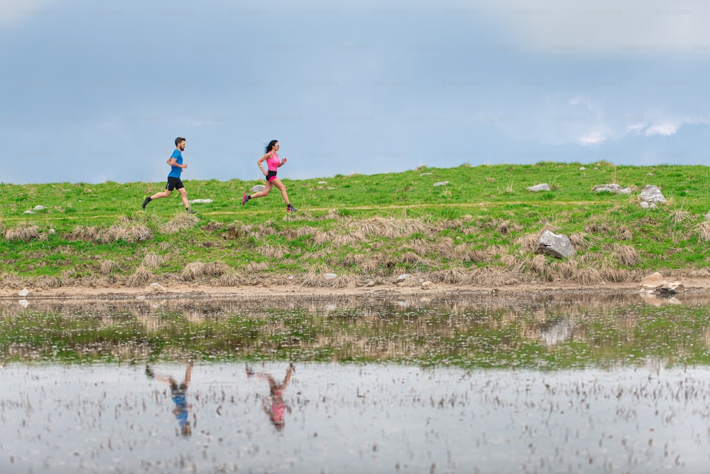 Athletes in training in the mountains are reflected in the lake as they run