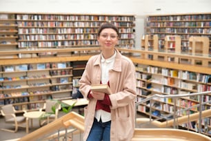 Retrato da mulher nova com o livro em pé na grande biblioteca