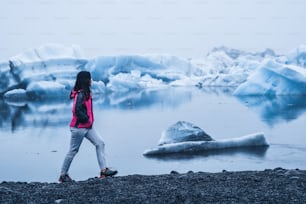 アイスランドのヨークルスアゥルロゥン美しい氷河ラグーンに旅行する女性旅行者。ヨークルスアゥルロゥンは、ヨーロッパのアイスランド南東部にあるヴァトナヨークトル国立公園の有名な観光地です。寒い冬の氷の自然。