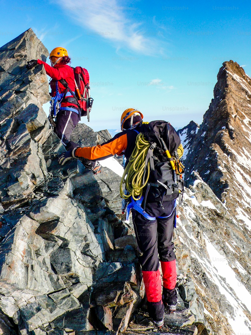 male and female mountain climber on an exposed rocky summit ridge on their way to a high alpine mountain peak near Zermatt in the Swiss Alps