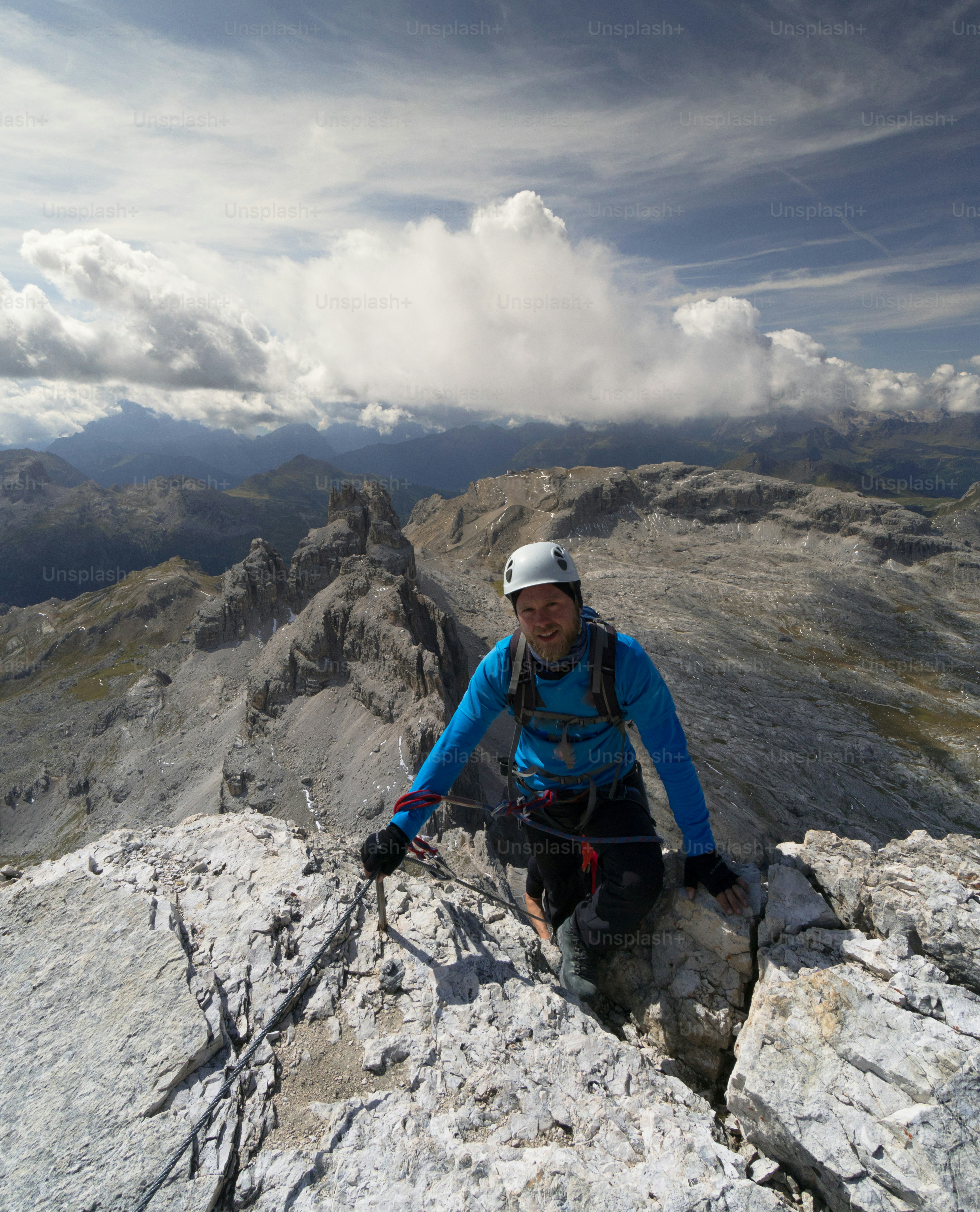 pendaki pria muda dengan jaket biru dan helm putih mencapai puncak dan ujung Via Ferrata di Tirol Selatan di Dolomites Italia