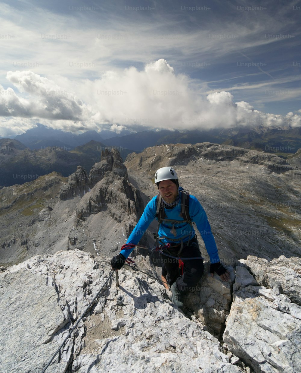 young male climber in a blue jacket and white helmet reaches the summit and end of a Via Ferrata in the South Tyrol in the Italian Dolomites