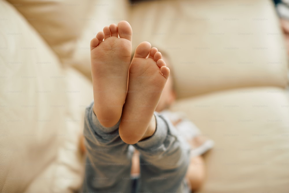 Primer plano de un niño pequeño que se relaja en el sofá con los pies hacia arriba. La atención se centra en los pies.