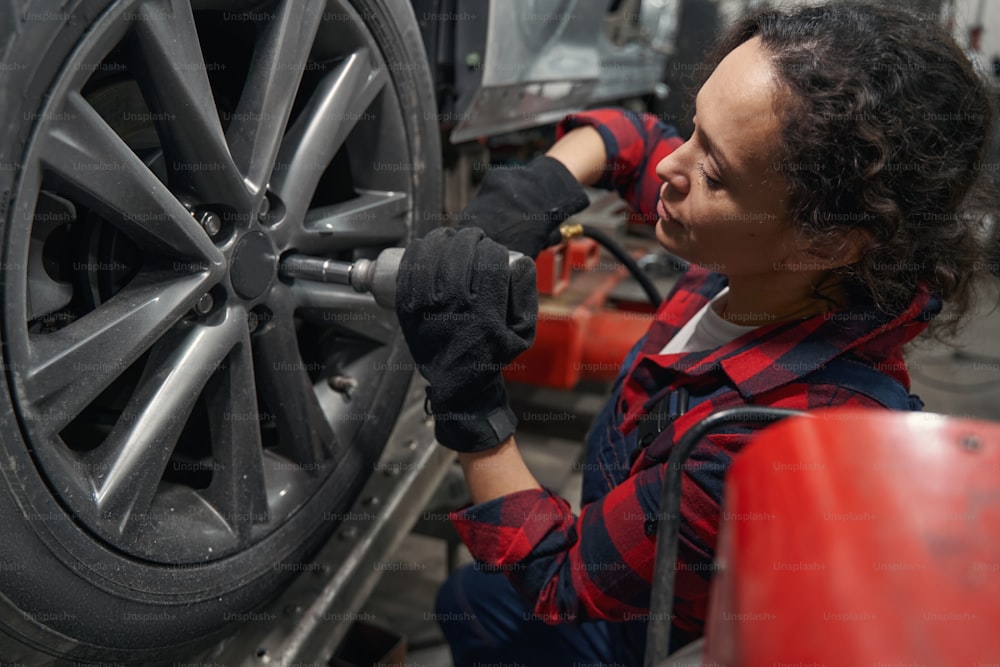 Mujer técnica de vehículos que arregla la rueda del automóvil en la estación de servicio de reparación