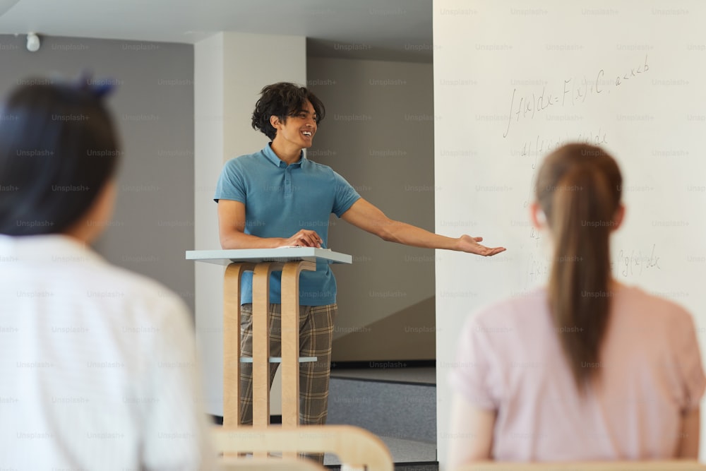 Cheerful student boy in casual outfit gesturing hand while presenting his research at university class