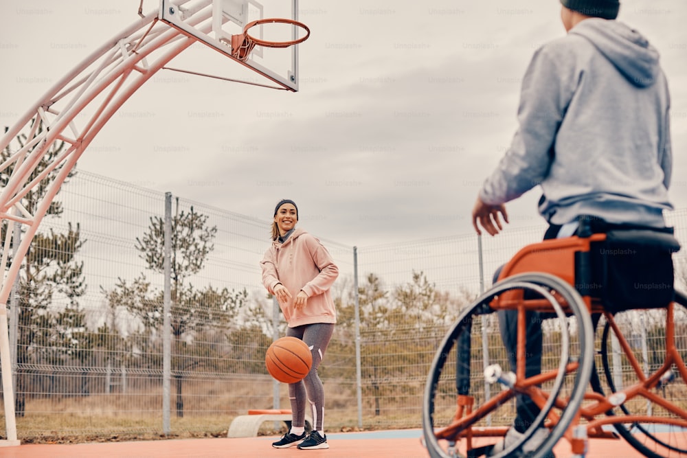 Young happy woman and her friend with disability enjoying in basketball game on outdoor court.