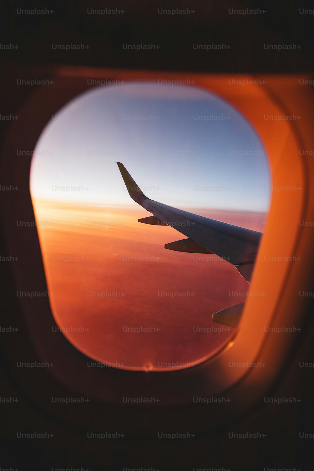 View from the window of the aircraft on the wing over the colorful sunset and illuminated vivid clouds