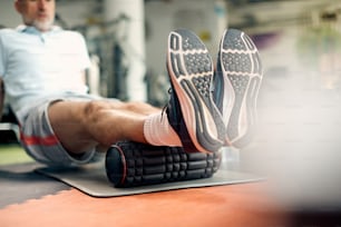Primer plano del uso del rodillo de espuma y el masaje de los músculos de las piernas durante el entrenamiento en el gimnasio.