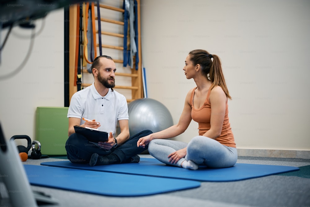Joven deportista y fisioterapeuta comunicándose mientras hace sus planes de entrenamiento en el centro de fisioterapia.