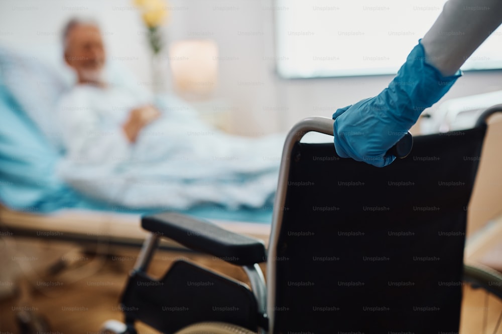 Primo piano del medico che spinge la sedia a rotelle mentre entra nella stanza del paziente in ospedale.