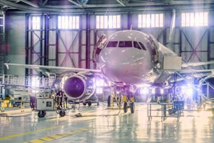 Avión civil en mantenimiento de reparación de motor y fuselaje en hangar del aeropuerto. Tinte púrpura claro brillante en la puerta