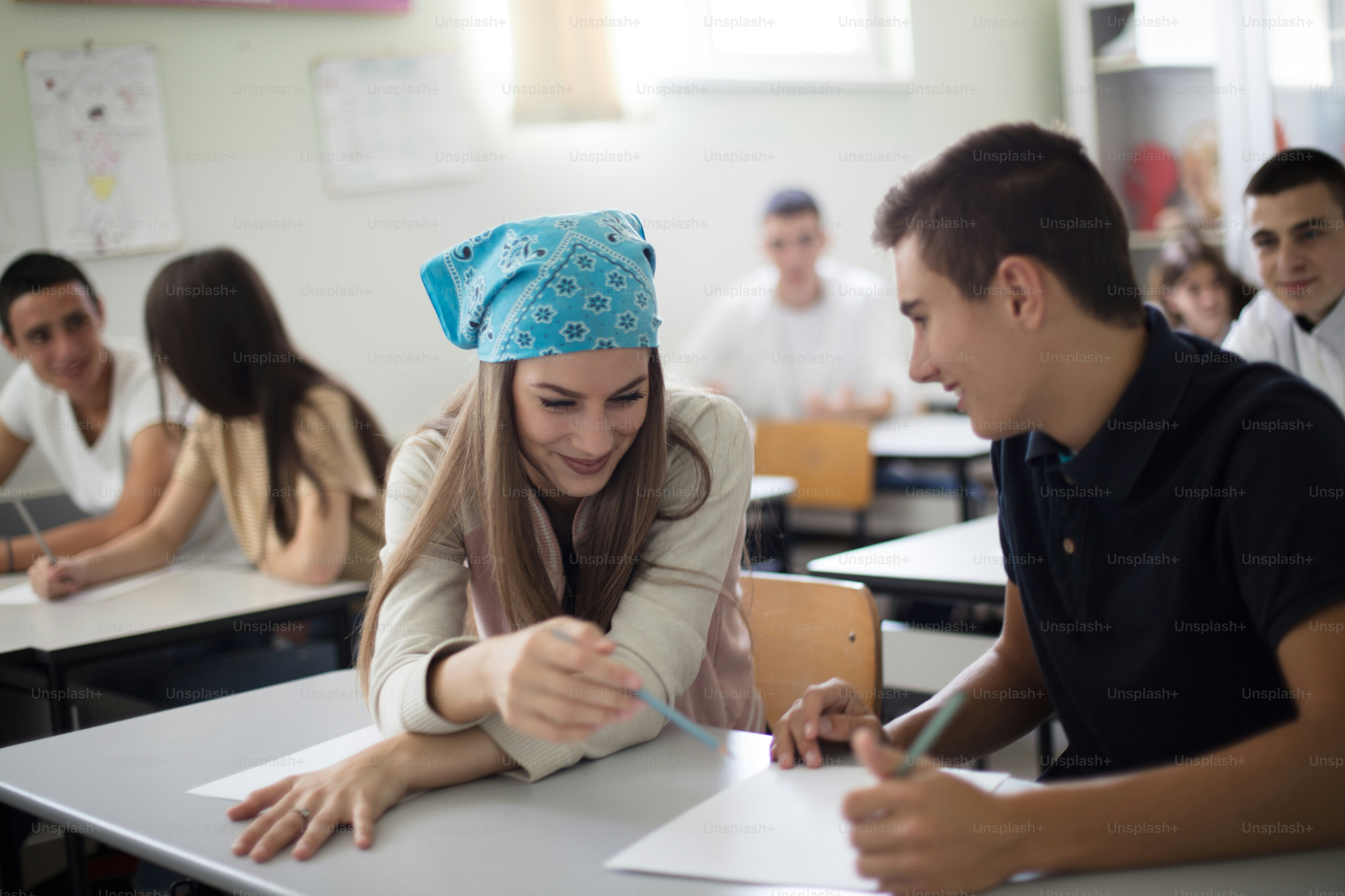 Tachonando juntos.  Estudiantes adolescentes sentados en el aula trabajando examen.