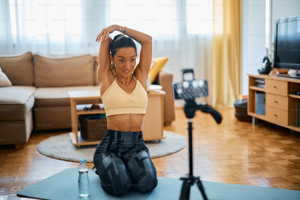 Fitness instructor warming up and stretching her arms while live streaming during home workout.