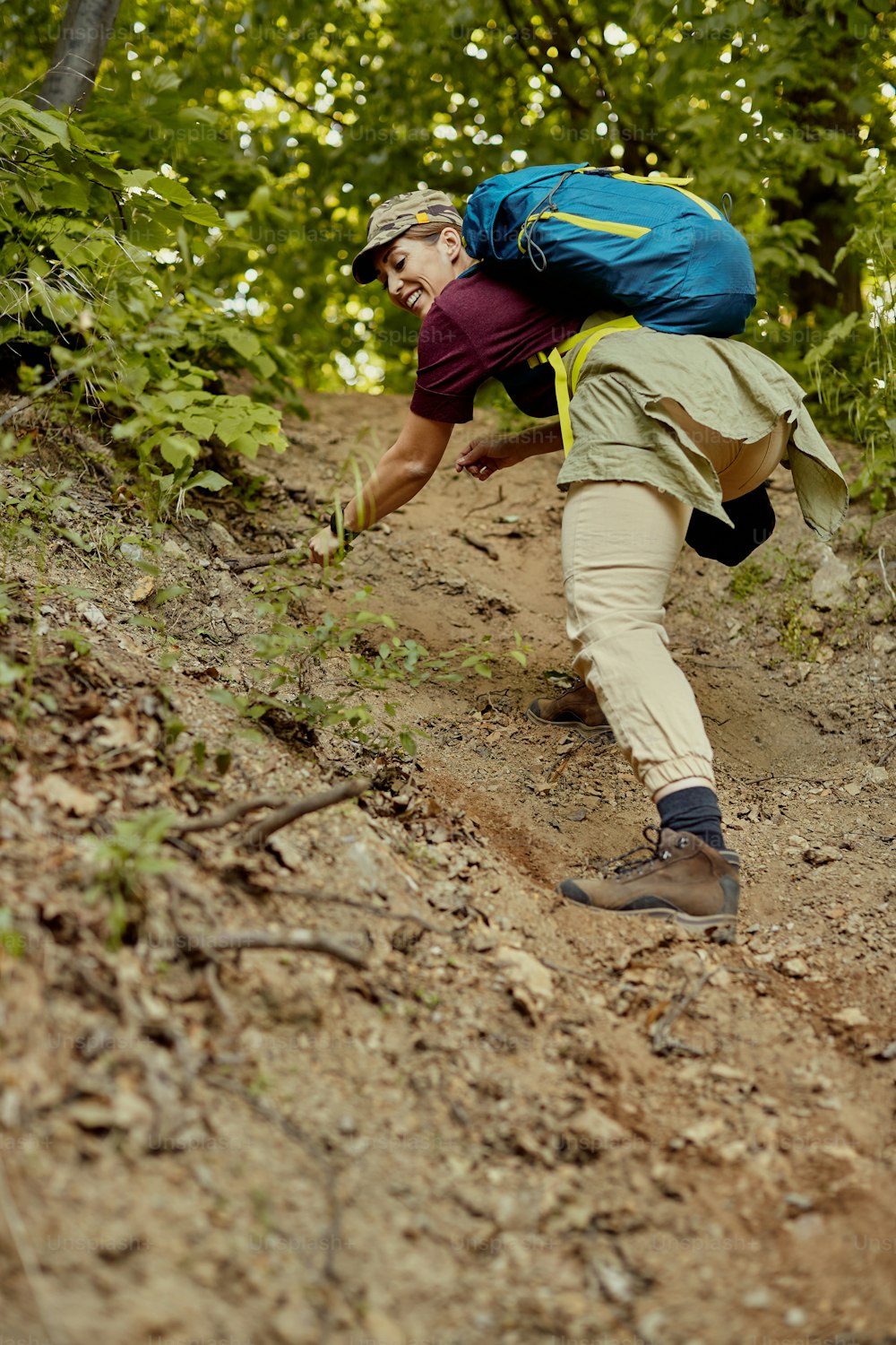 Low angle view of happy hiker with backpack climbing up along dusty forest trail. Copy space.