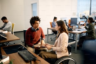 Une femme d’affaires en fauteuil roulant et son collègue afro-américain communiquent tout en travaillant dans une entreprise de développement de logiciels.