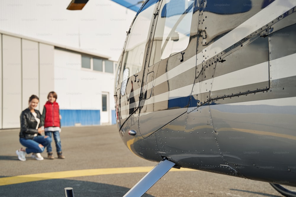 Young woman squatting near her little son while looking at shiny helicopter