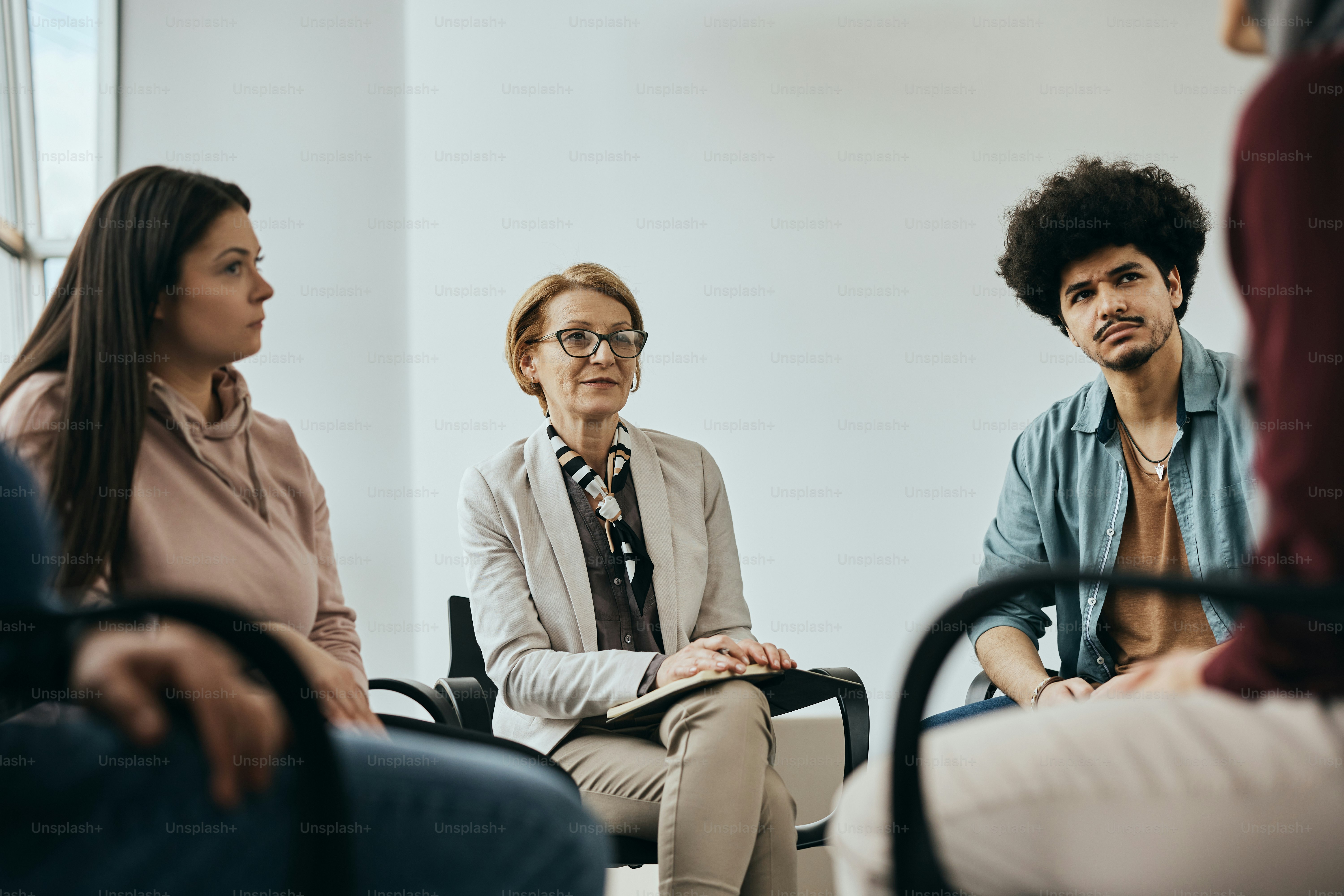 Mature therapist listening her patients during group therapy session at mental health center.