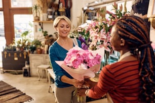 꽃집에서 고객에게 신선한 꽃다발을 주는 아프리카계 미국인 꽃집. 여성 고객에게 초점을 맞춥니다.