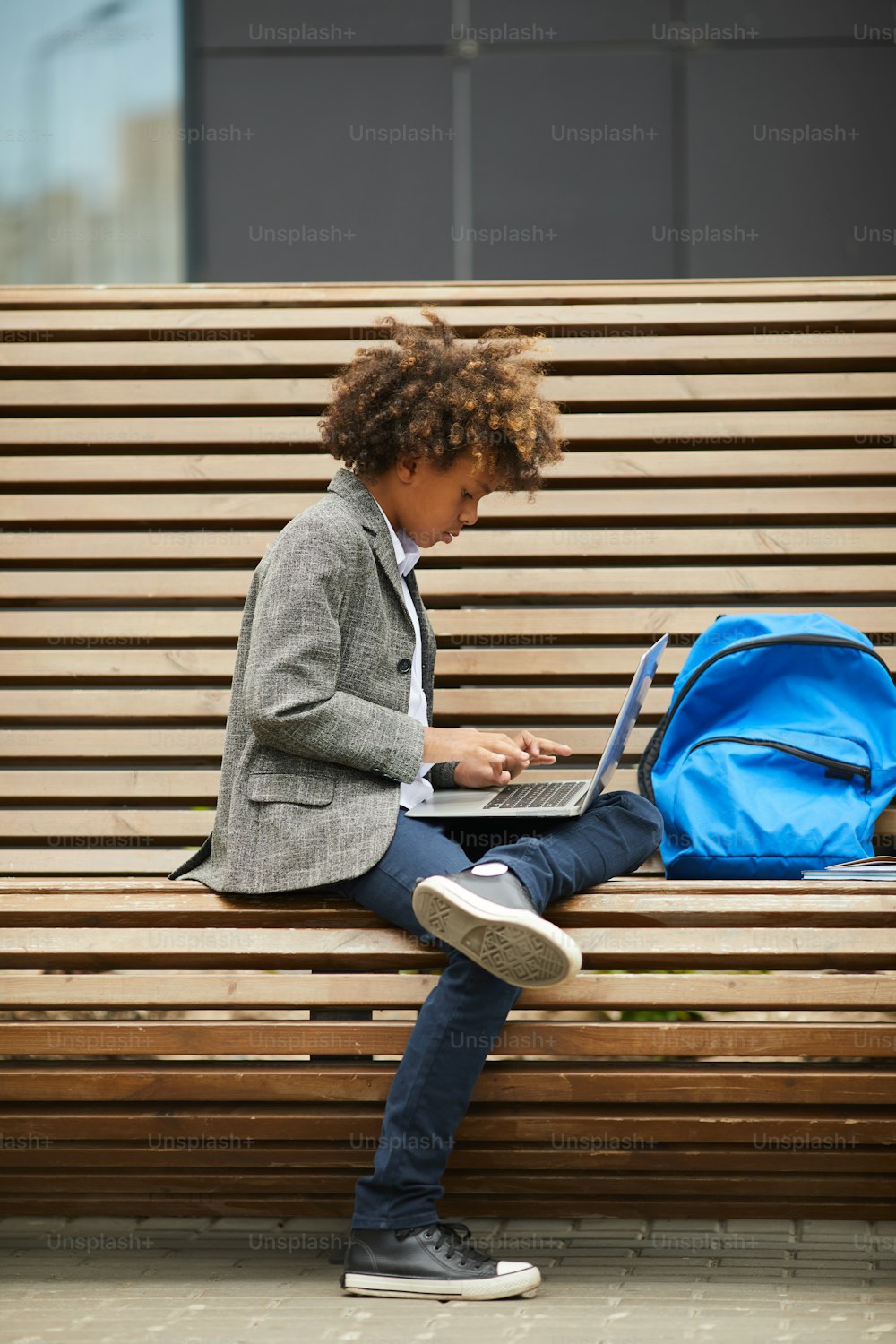 Écolier africain assis seul sur le banc et tapant sur son ordinateur portable, il fait ses devoirs à l’extérieur