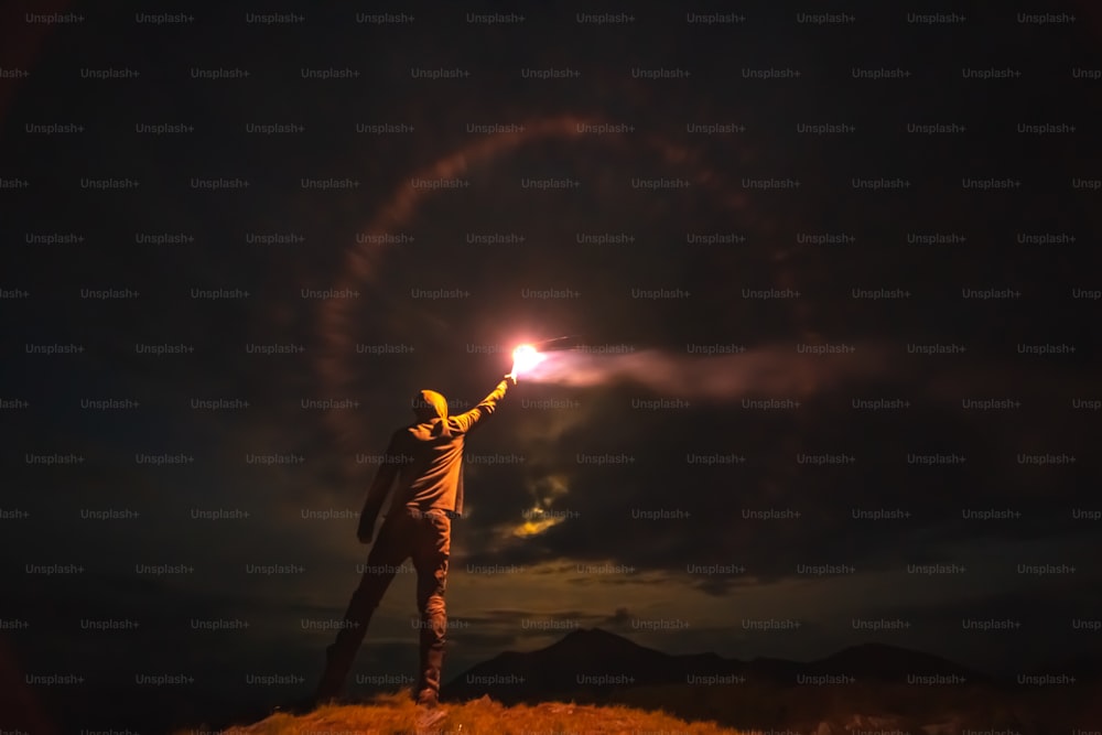 Der Mann mit einem hellen Feuerwerksstab steht auf einem Berg. Abend Nacht