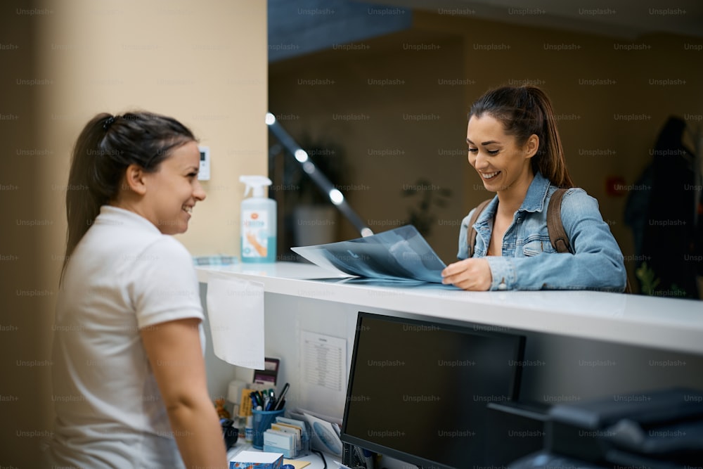 Happy patient examining her X-ray scan at physical therapy reception desk.