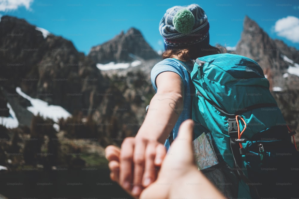 Young active hiking couple with backpacks taking photo, woman guiding by the hand into mountain wilderness