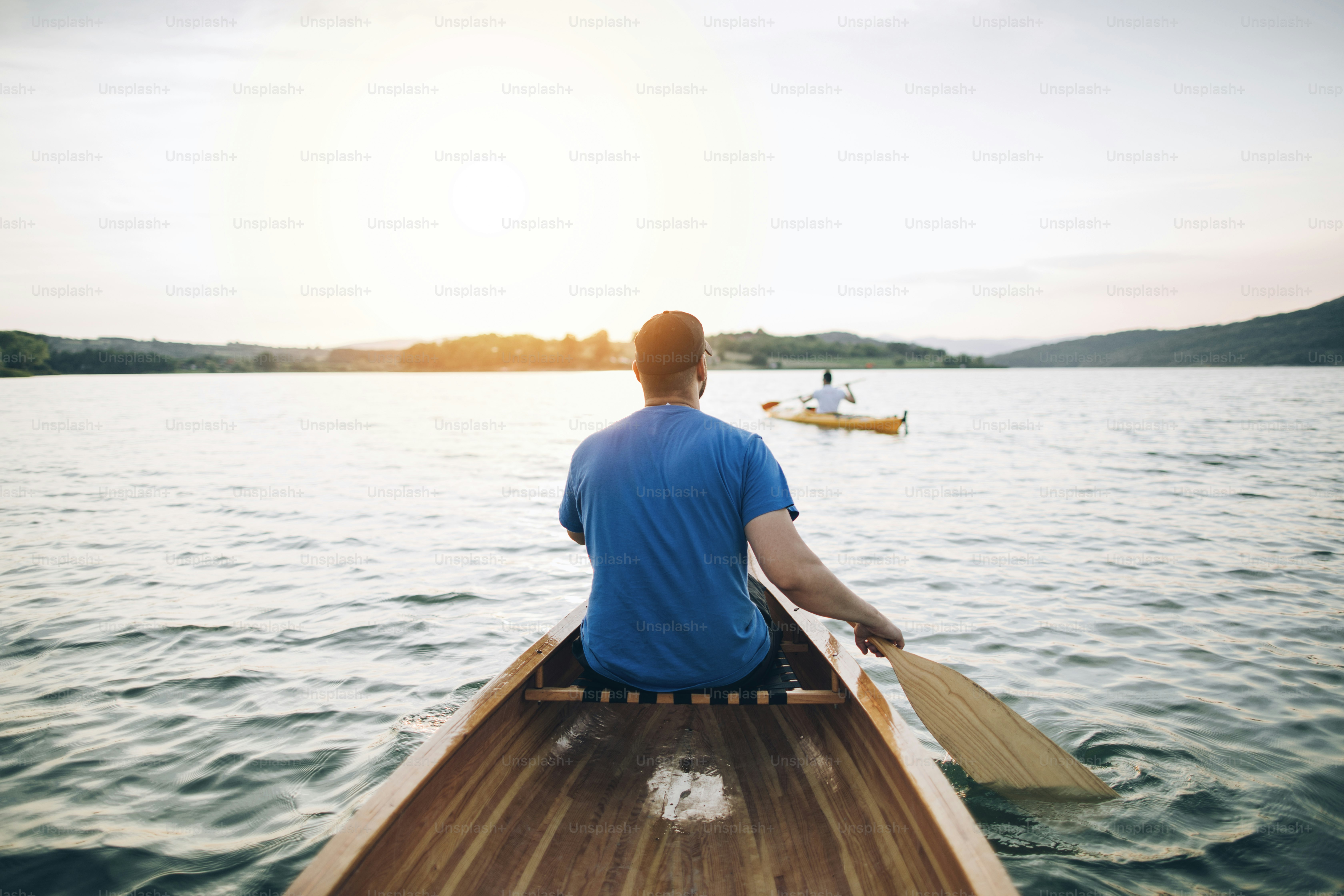 Rear view of men paddling canoe and kayak at sunset lake. photo ...
