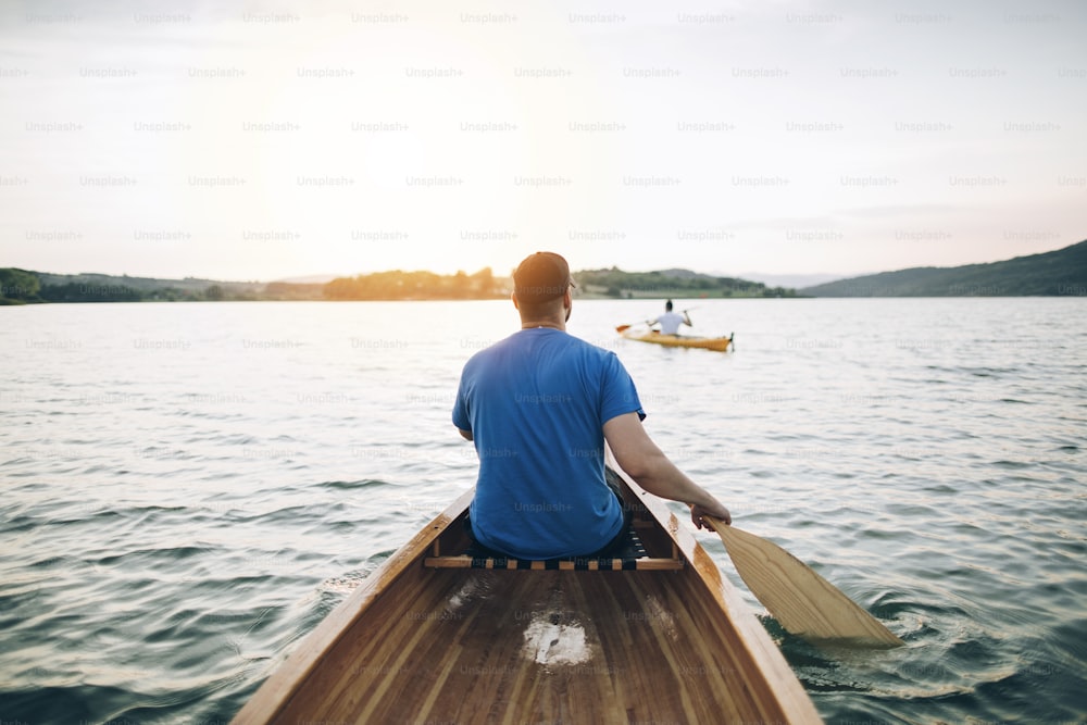 Vista posteriore di uomini che remano in canoa e kayak al tramonto sul lago.