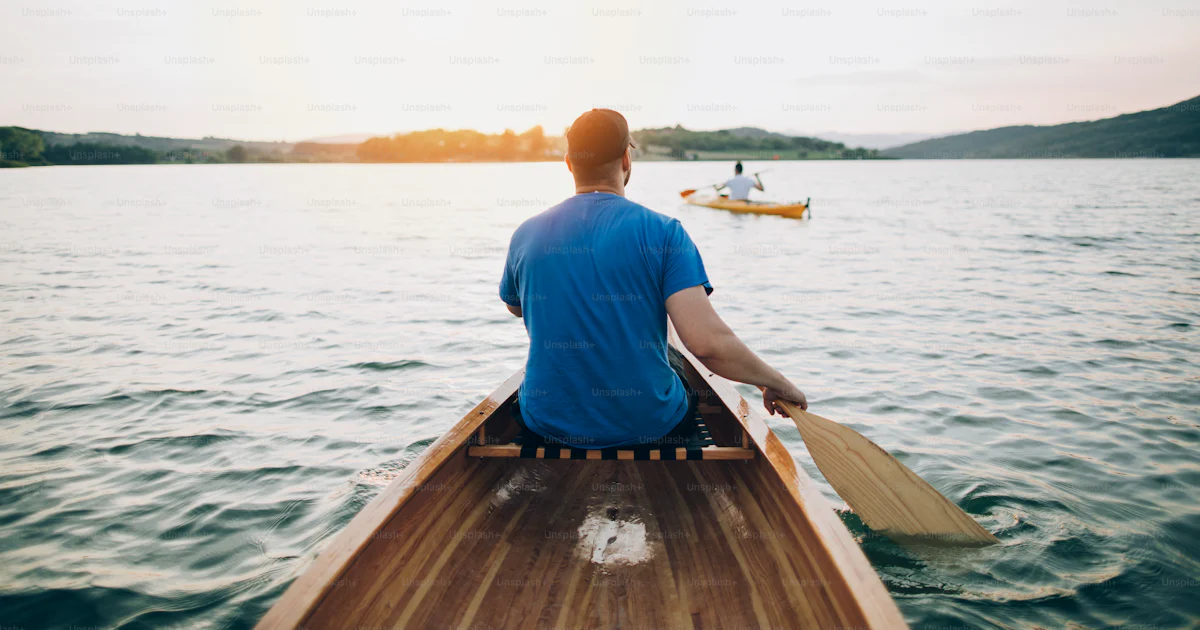 Rear view of men paddling canoe and kayak at sunset lake. photo ...