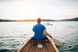 Rear view of men paddling canoe and kayak at sunset lake.