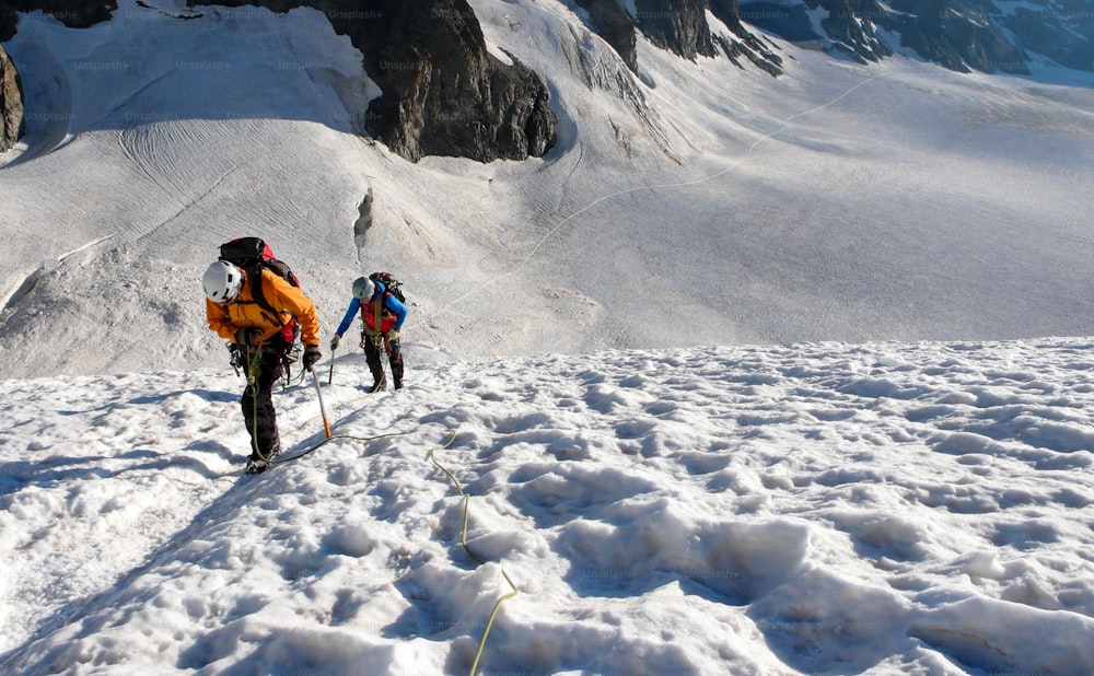 Guía de montaña y cliente subiendo un glaciar hacia una alta cumbre alpina en una hermosa mañana de verano en los Alpes franceses