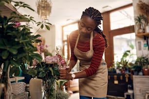 Mulher afro-americana jovem que organiza flores frescas enquanto trabalha na floricultura.