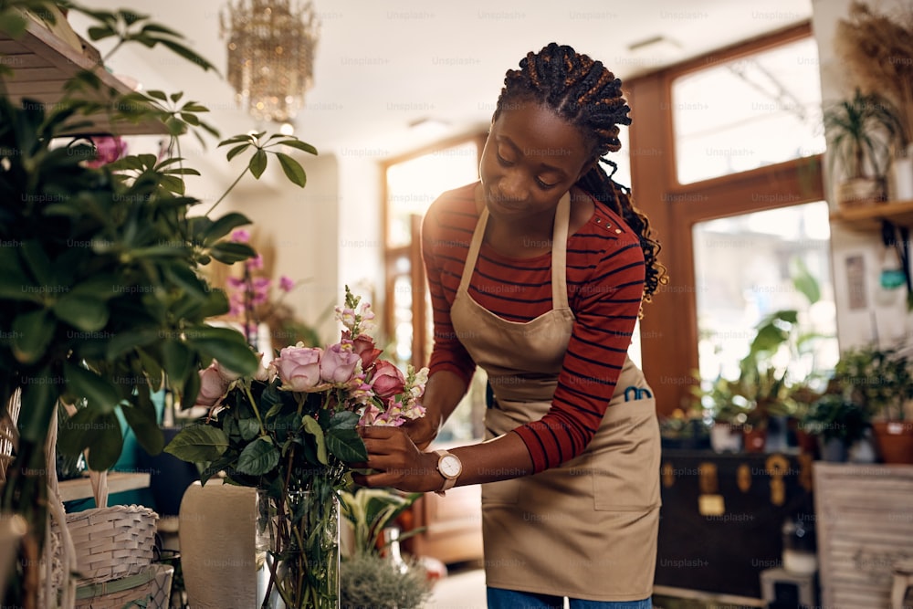Young African American woman arranging fresh flowers while working at flower shop.